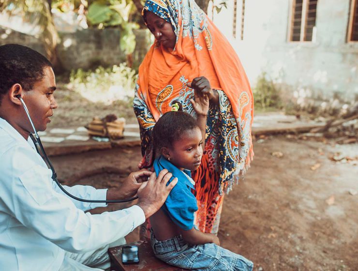 A doctor uses a stethescope to examine a child in Africa, as the child's mother stands nearby.