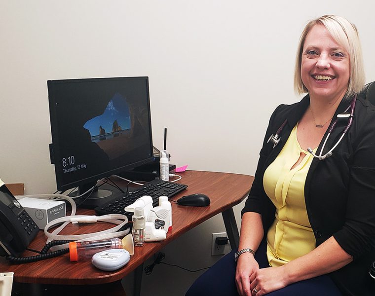 Karen McElroy sits next to a computer with respiratory devices on the desk.