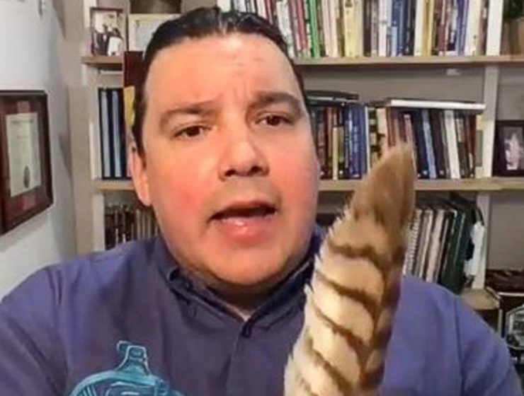 Niigaan Sinclair holding a feather during a virtual presentation.